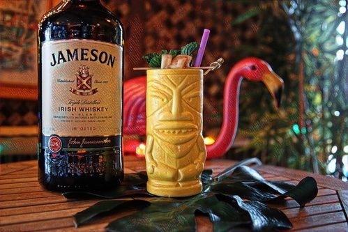 jameson whiskey bottle next to yellow tiki mug with fruit garnish
