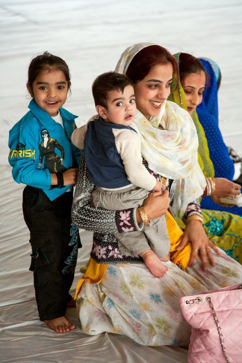 One women holding a child in the foreground, with another woman and a child standing in the background.
