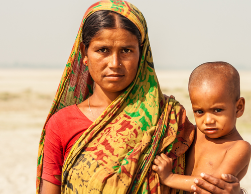 A photo of a Bangladeshi family of four. The father is holding the son, and the mother is holding a sleeping infant.